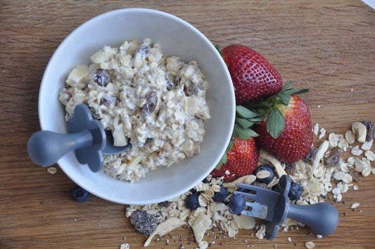 bowl of overnight oats with a grabease spoon. Surrounded by strawberries, blueberries and dry oats as well as a grabease fork.