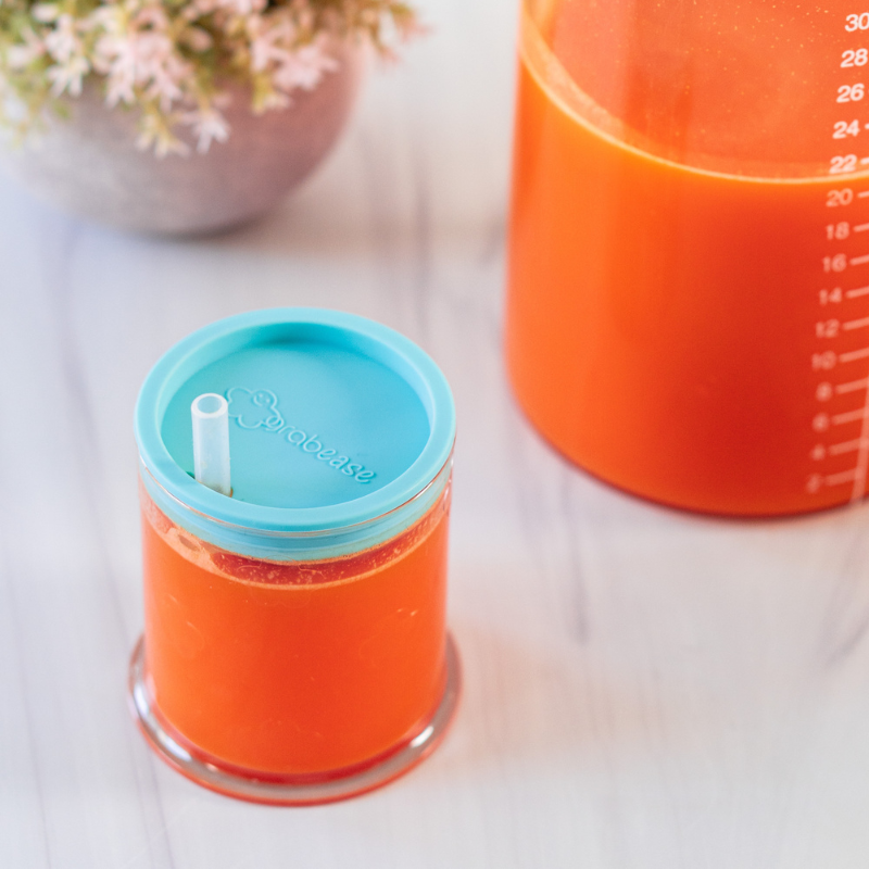 Carrot juice served in a teal grabease baby cup with straw